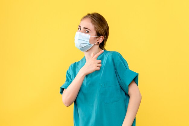 黄色の背景の健康病院パンデミックcovidのマスクで正面図の女性医師