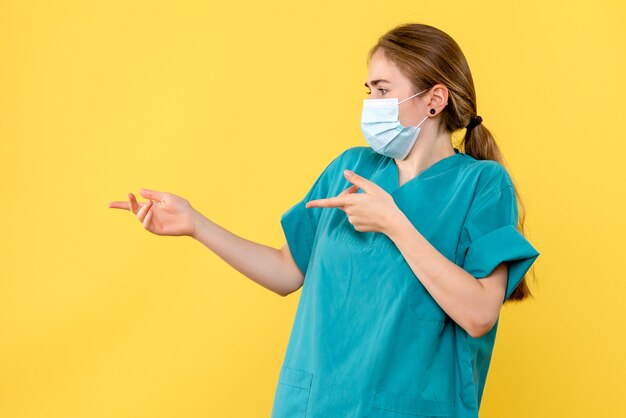 Front view female doctor in mask on yellow background pandemic covid virus