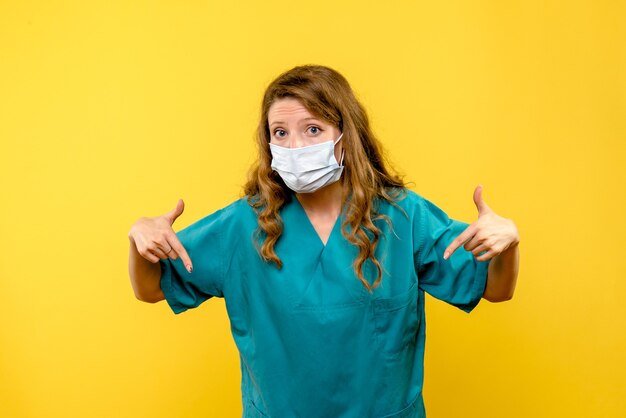 黄色い床の薬の健康covidパンデミックのマスクの女医の正面図