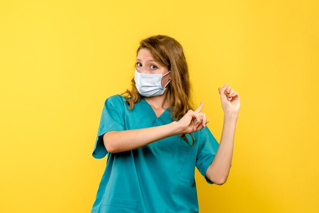 Front view female doctor in mask on a yellow space