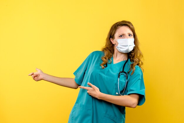 Front view female doctor in mask on the yellow space