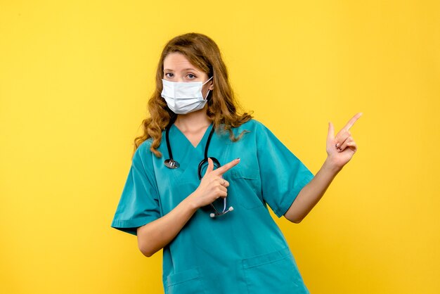 Front view of female doctor in mask on yellow wall