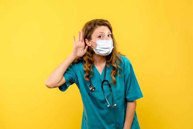 Front view of female doctor in mask on yellow wall