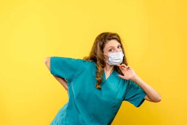 Front view of female doctor in mask on yellow wall