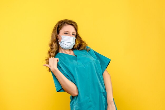 Front view of female doctor in mask on yellow wall