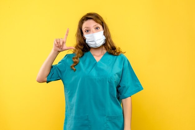 Front view of female doctor in mask on yellow wall