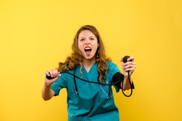 Front view of female doctor measuring pressure on light yellow wall