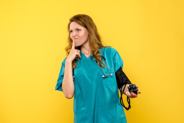 밝은 노란색 벽에 압력을 측정하는 여성 의사의 전면보기