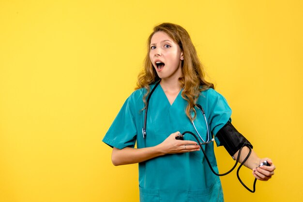 Front view of female doctor measuring pressure on yellow wall