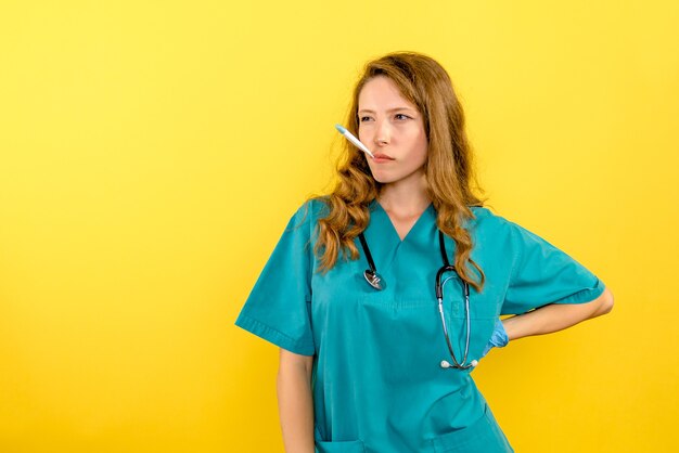 Front view of female doctor measuring temperature on yellow wall