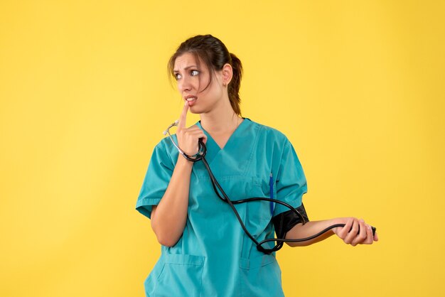 Front view female doctor in medical shirt checking her pressure on yellow background