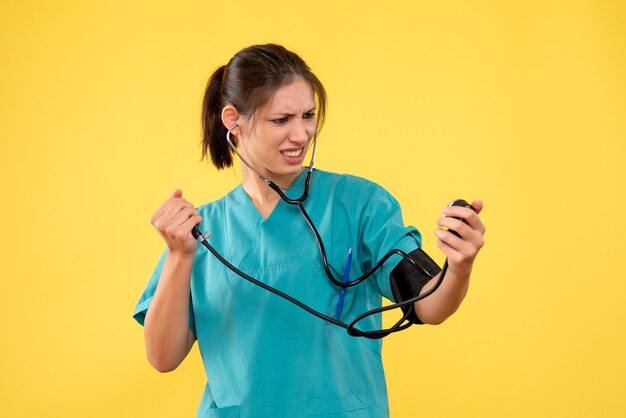 Front view female doctor in medical shirt checking her pressure on yellow background