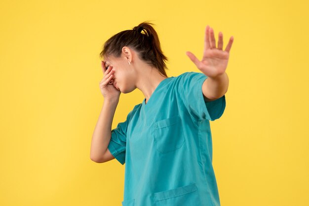 Вид спереди женщина-врач в медицинской рубашке, закрывая лицо на желтом фоне