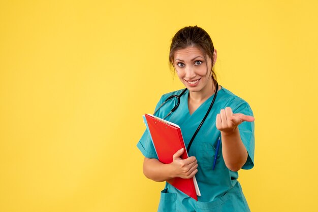 Front view female doctor in medical shirt holding analysis on yellow background