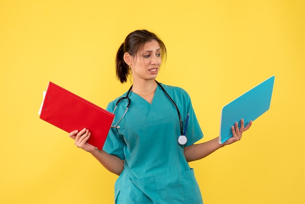 Front view female doctor in medical shirt holding analysis on yellow background
