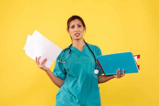 Front view female doctor in medical shirt holding analysis on yellow background