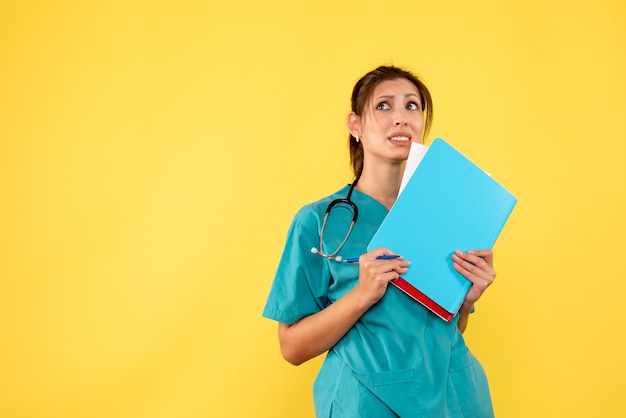 Front view female doctor in medical shirt holding analysis on yellow background