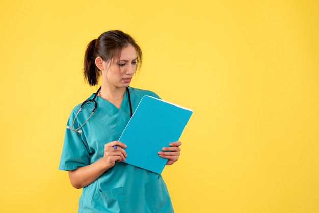 Front view female doctor in medical shirt holding analysis on yellow background