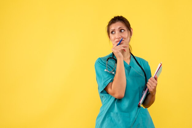 Free photo front view female doctor in medical shirt holding analysis on yellow desk virus health color covid- emotion medic hospital