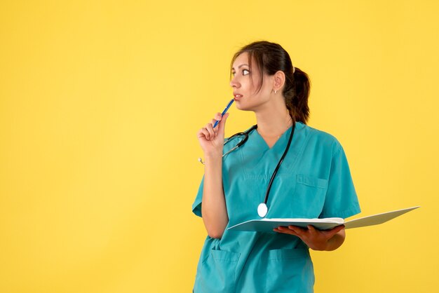 Front view female doctor in medical shirt holding notes on yellow background