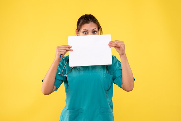 Вид спереди женщина-врач в медицинской рубашке, держащая анализ бумаги на желтом фоне