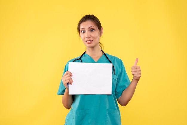 Вид спереди женщина-врач в медицинской рубашке, держащая анализ бумаги на желтом фоне