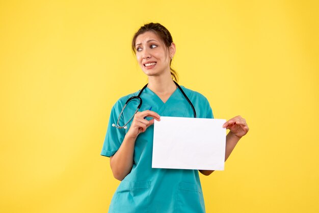 Front view female doctor in medical shirt holding paper analysis on yellow background