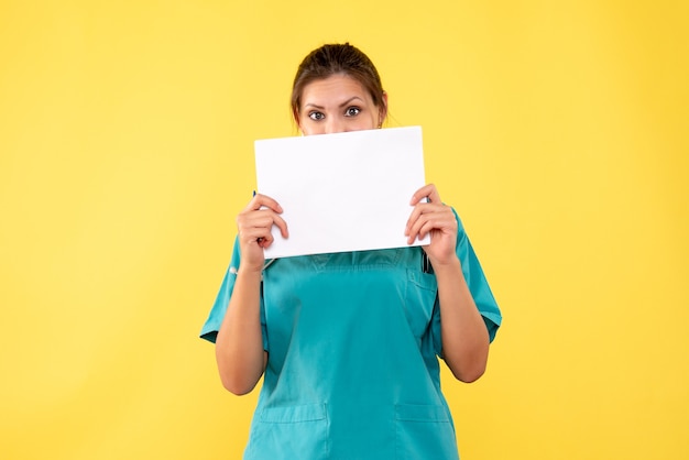 Front view female doctor in medical shirt holding paper analysis on yellow background