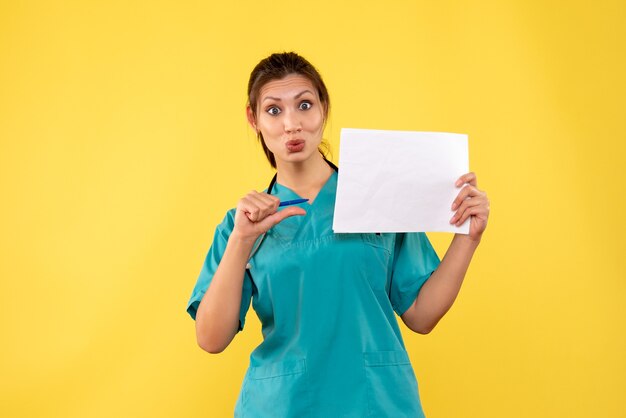 Front view female doctor in medical shirt holding paper analysis on yellow background