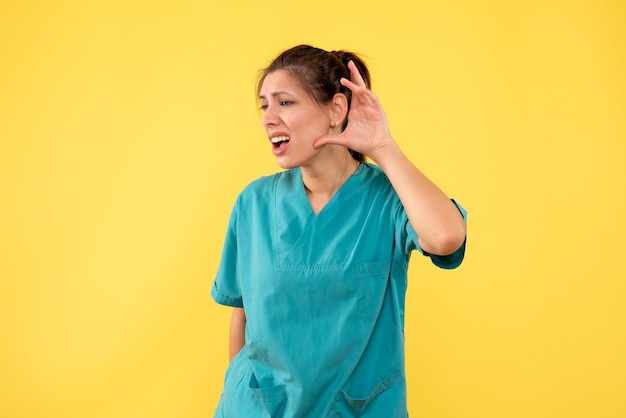 Front view female doctor in medical shirt listening on yellow background