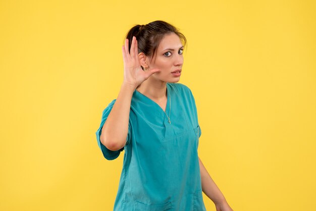 Front view female doctor in medical shirt listening on yellow background