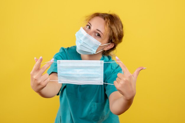 Front view female doctor in medical shirt mask and holding another mask, color covid-19 virus health emotion pandemic