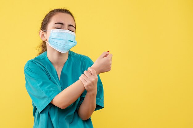 Front view female doctor in medical shirt and mask with hurt arm, color pandemic health virus covid-19 uniform