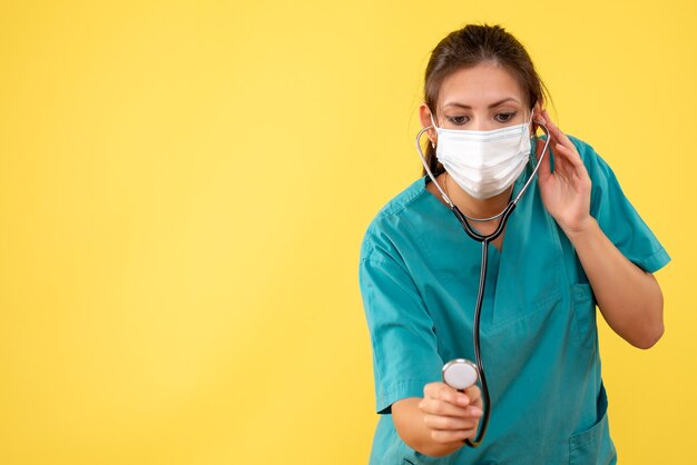 Medico femminile di vista frontale in camicia medica e maschera con lo stetoscopio su fondo giallo