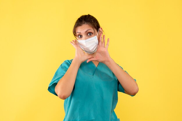 Front view female doctor in medical shirt and mask on the yellow background