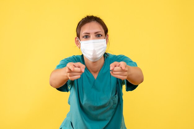 Front view female doctor in medical shirt and mask on yellow background