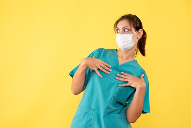 Front view female doctor in medical shirt and mask on yellow background