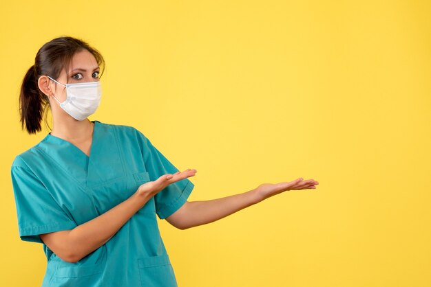 Front view female doctor in medical shirt and mask on yellow background