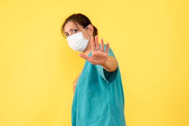 Front view female doctor in medical shirt and mask on yellow background