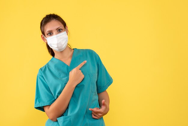 Front view female doctor in medical shirt and mask on yellow background