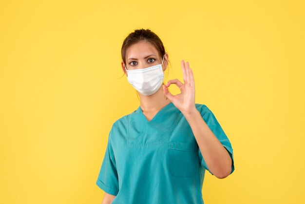 의료 셔츠와 노란색 배경에 마스크에 전면보기 여성 의사