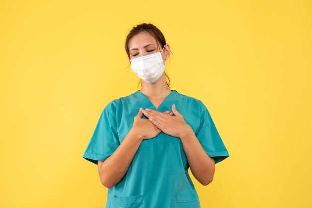 Front view female doctor in medical shirt and mask on yellow background