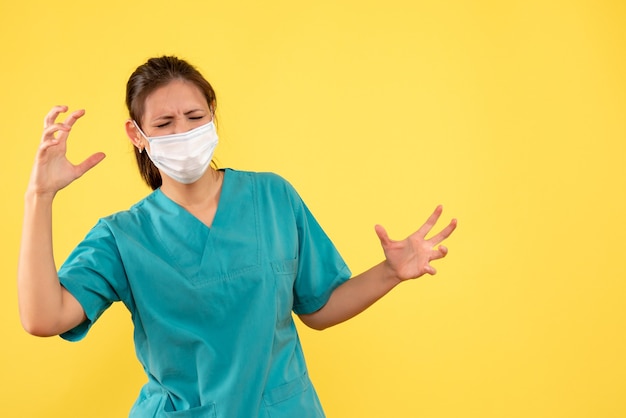 Front view female doctor in medical shirt and mask on yellow background