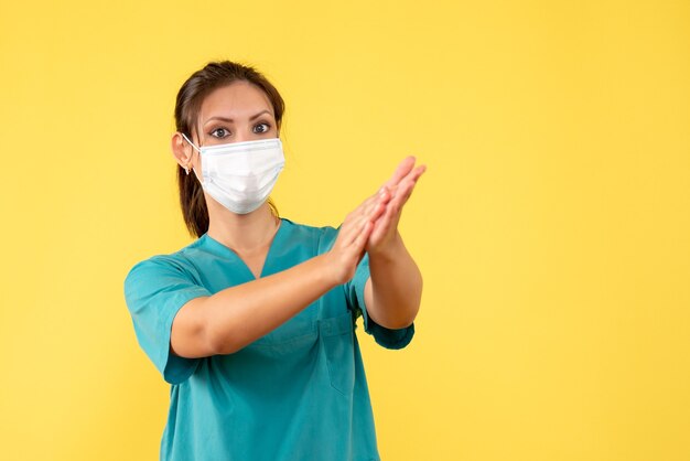 Front view female doctor in medical shirt and mask on yellow background