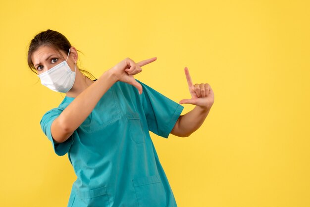 Front view female doctor in medical shirt and mask on yellow background