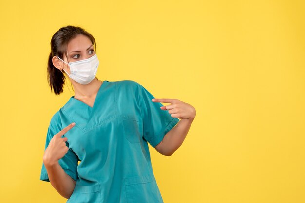 Front view female doctor in medical shirt and mask on yellow background