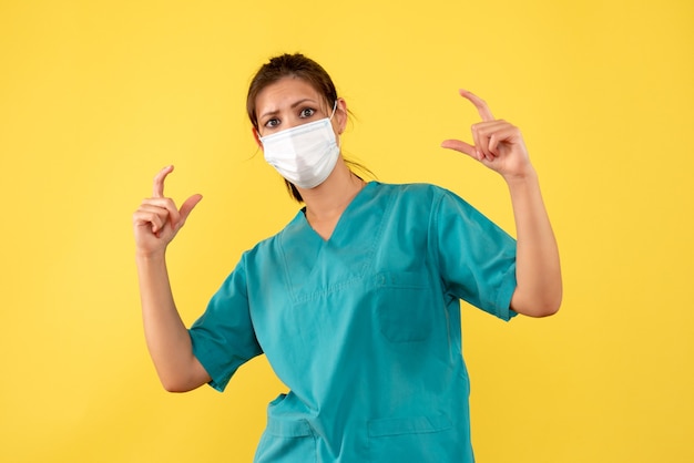 Вид спереди женщина-врач в медицинской рубашке и маске на желтом фоне