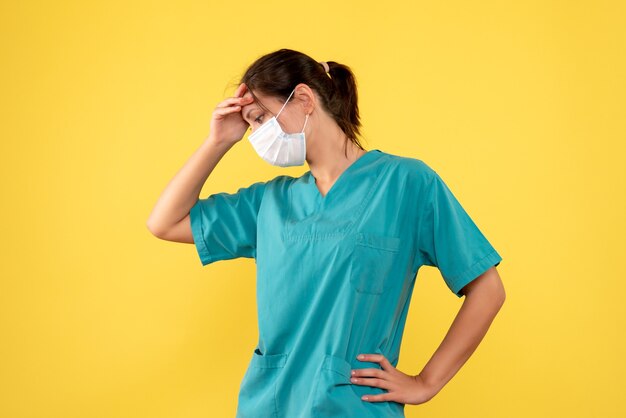 Front view female doctor in medical shirt and mask on yellow background