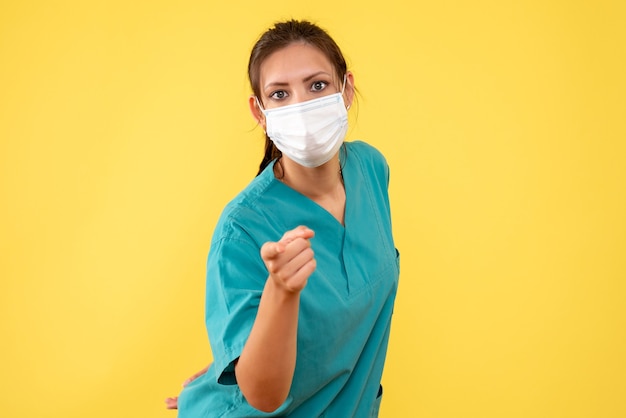 의료 셔츠와 노란색 배경에 마스크에 전면보기 여성 의사