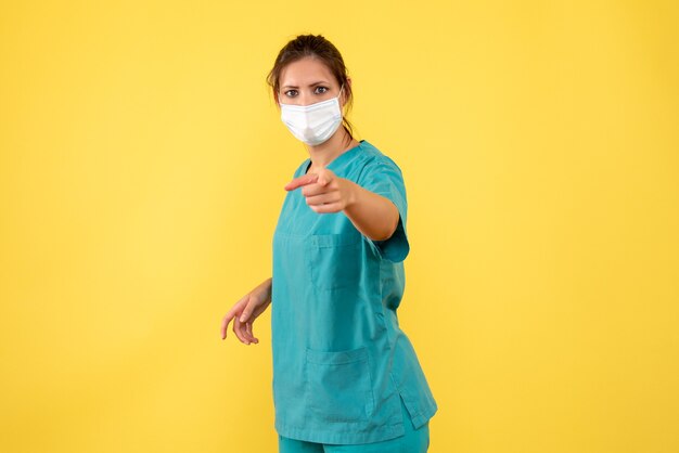 Front view female doctor in medical shirt and mask on yellow background